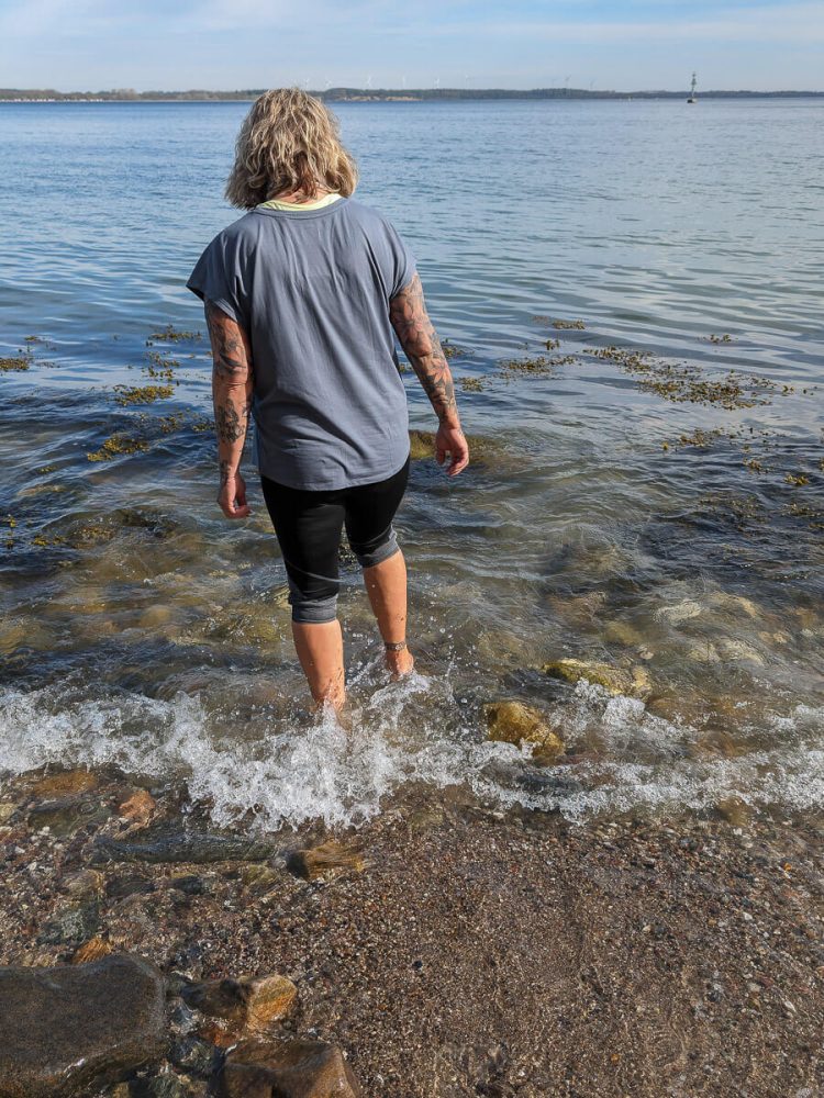 Frau steht barfuß im Meer