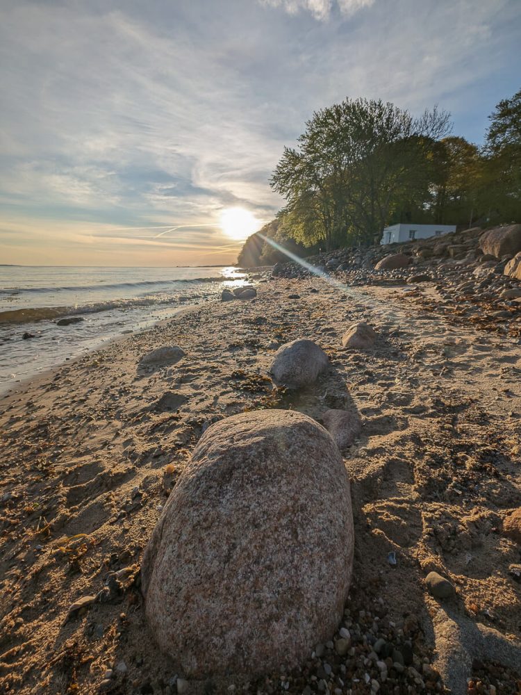 Großer Stein am Strand mit Sonnenaufgang im Hintergrund